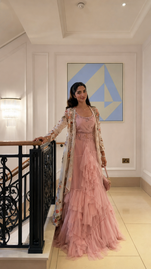Woman wearing a blush pink ruffle maxi gown with a sheer floral embroidered long cape