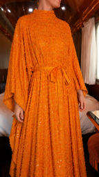 Close-up of orange textured shimmer maxi dress with self-tie belt and draped sleeve