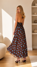 Angled back view of chocolate brown maxi dress with blue polka dots and flared hem